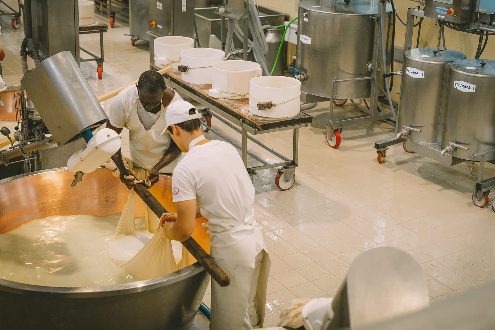 Deux employés en tenue d'hygiène blanche travaillent au-dessus d'une cuve dans une usine de transformation alimentaire.