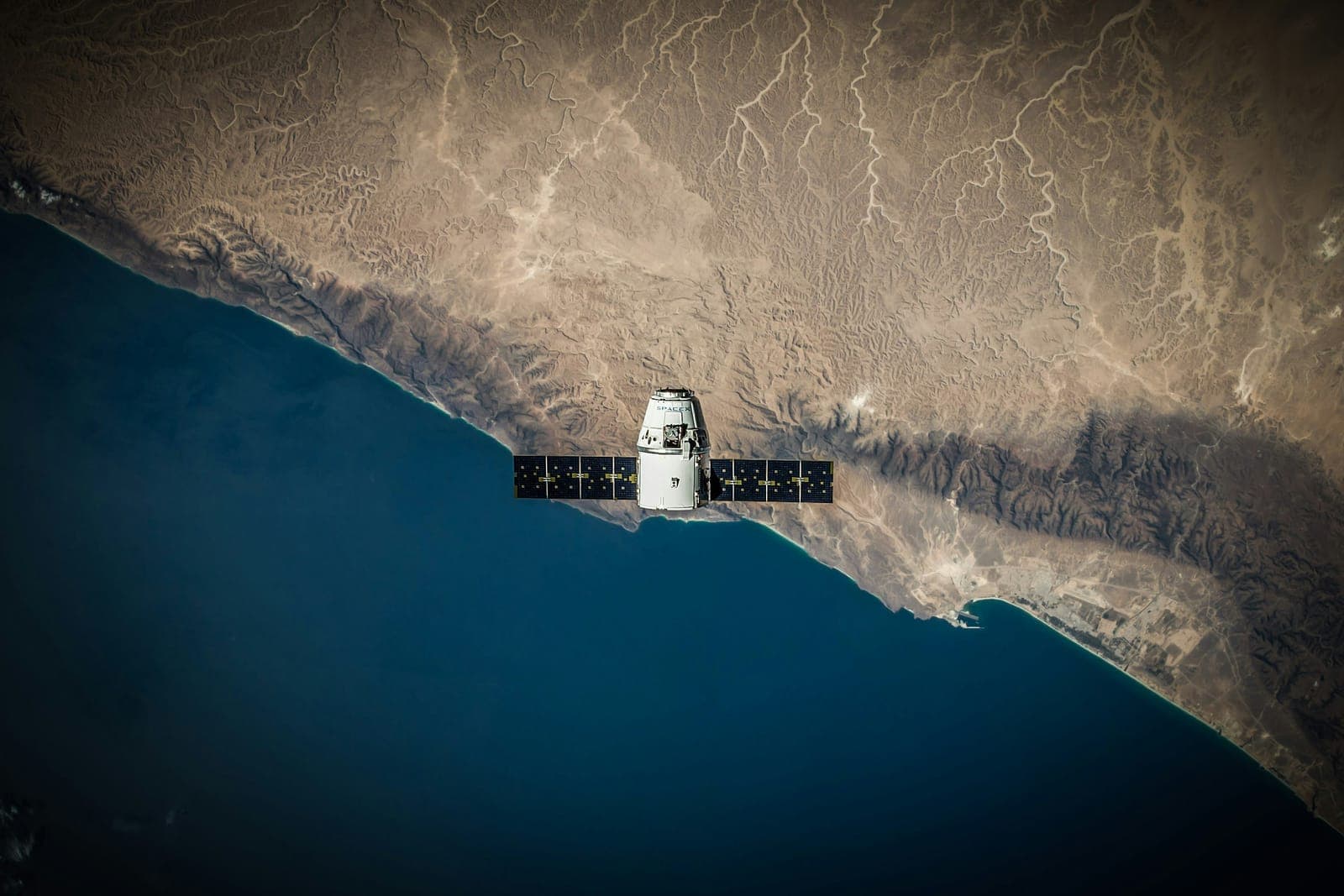 Satellite en orbite basse au-dessus d'une côte, panneaux solaires déployés.