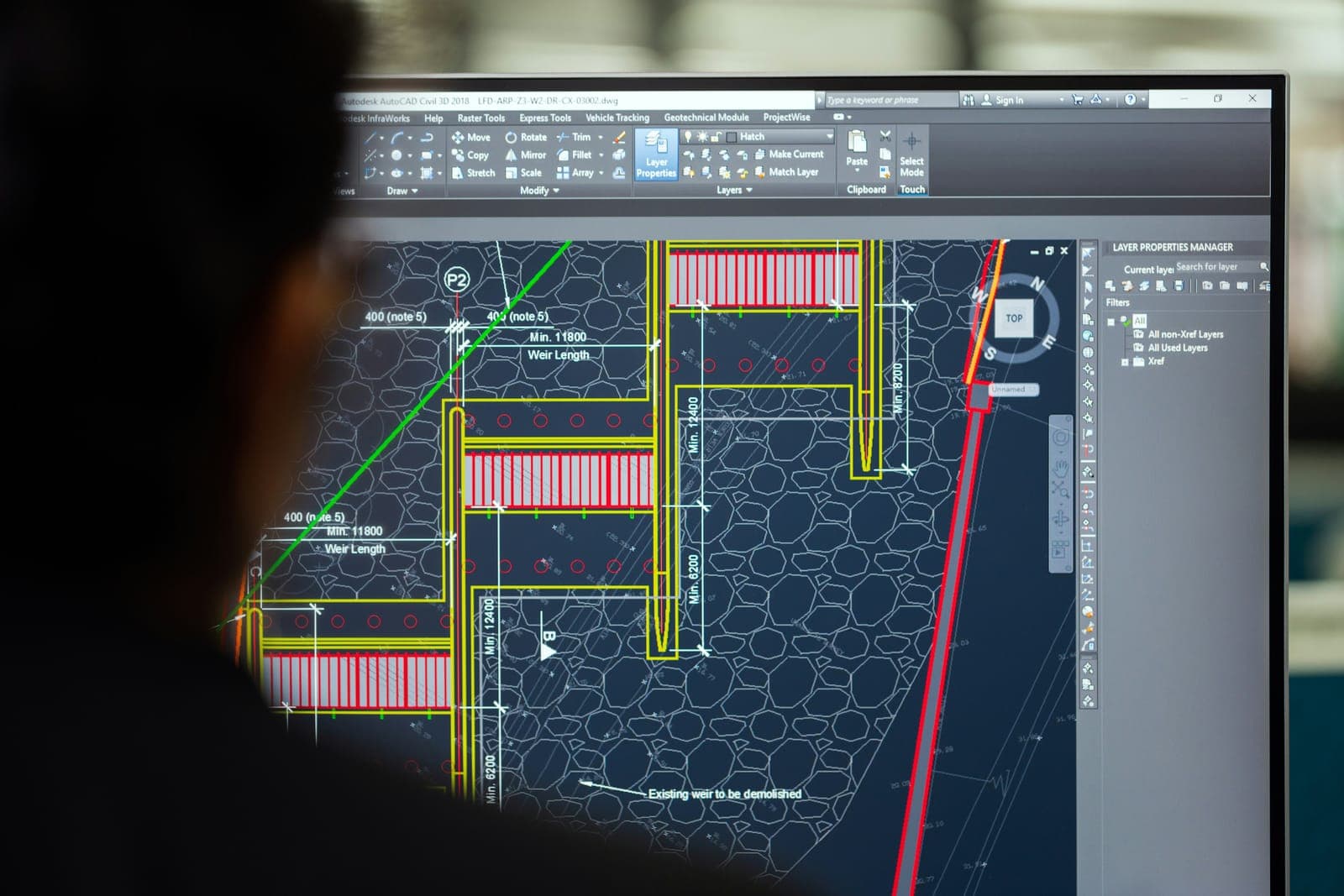Ingénieur devant un écran affichant un plan technique dans un logiciel de conception assistée par ordinateur.